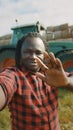 Video call. African farmer waving to the smartphone camere in front of the tractor Royalty Free Stock Photo