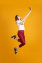 Full length portrait of young Caucasian girl jumping with phone isolated on yellow studio background. Concept of human Royalty Free Stock Photo