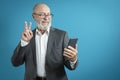 Video call by phone. Handsome elderly man greets a friend using a mobile phone in a classic suit on a blue background. studio