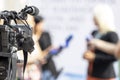 Video camera in focus, blurred journalists at news conference holding microphones making media interview with female politician Royalty Free Stock Photo