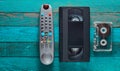Video cassette, audio cassette, remote control on a turquoise wooden table. Retro media technology from the 80s. Copy space. Top v