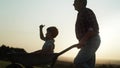 Video of grandfather driving grandson in wheelbarrows at sunset.