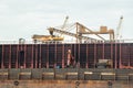 Loading coal from cargo barges onto a bulk carrier using ship cranes.