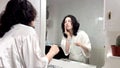 video of portrait of a latin woman holding a toothbrush looking at her molars and teeth in the mirror.