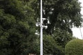 Video surveillance camera and two loud speakers on metallic pole with green foliage on background. Royalty Free Stock Photo