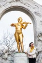 Tourist being photographed next to the Monument to Johann Strauss II at Stadtpark in a cold early spring day