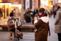 Asian tourist filming a street musician playing accordion in Vienna Kaernter Strasse on a cold day in winter