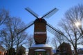 View over snow on red green colorfull striped wind mill Narrenmuhle with bare trees, sun lens flares