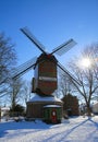 View over snow on red green colorfull striped wind mill Narrenmuhle with bare trees, sun lens flares