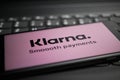 Close up of mobile phone screen with logo lettering of Klarna payment provider on computer keyboard