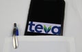 Close up of mobile phone screen with logo lettering of Teva pharmaceutical company in pocket of white doctors coat with pencil