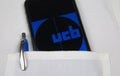 Close up of mobile phone screen with logo lettering of UCB pharmaceutical company in pocket of white doctors coat with pencil