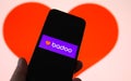 Closeup of mobile phone screen with logo lettering of online dating agency app badoo, blurred heart background