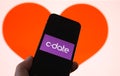 Closeup of mobile phone screen with logo lettering of online dating agency app c-date, blurred heart background