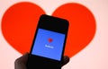 Closeup of mobile phone screen with logo lettering of online dating agency app facebook, blurred heart background