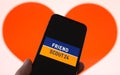 Closeup of mobile phone screen with logo lettering of online dating agency app friendscout24, blurred heart background