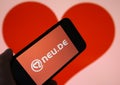 Closeup of mobile phone screen with logo lettering of online dating agency app neu.de, blurred heart background