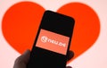 Closeup of mobile phone screen with logo lettering of online dating agency app neu.de, blurred heart background