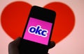 Closeup of mobile phone screen with logo lettering of online dating agency app okc, blurred heart background