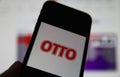 Closeup of smartphone screen with logo lettering of german otto mail order company, blurred website background
