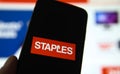 Closeup of smartphone screen with logo lettering of staples office supplies, blurred website background Royalty Free Stock Photo