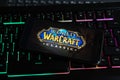 Closeup of smartphone screen with logo lettering of online game world of warcraft on illuminated computer keyboard