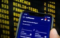 Closeup of mobile phone with Lufthansa flight booking app. Blurred departure board background. Royalty Free Stock Photo