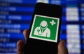 Viersen, Germany - July 9. 2020: View on hand holding mobile phone with green sign for health and medical assistance at airport.