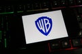 Closeup of mobile phone screen with logo lettering of film production company warner brothers on computer keyboard