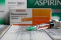 Closeup of covid-19 vaccine syringe with packets of aspirin, ibuprofen and aspirin for treatment of vaccination side effects and r