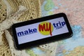 Closeup of mobile phone screen wit logo lettering of online booking travel agency makemytrip.com with sun hat and map Royalty Free Stock Photo