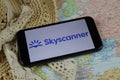 Closeup of mobile phone screen wit logo lettering of online booking travel agency skyscanner with sun hat and map Royalty Free Stock Photo