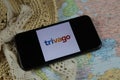 Closeup of mobile phone screen wit logo lettering of online booking travel agency trivago with sun hat and map