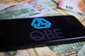 Closeup of smartphone with logo lettering of australian qbe insurance company on paper money currency Royalty Free Stock Photo