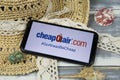 Closeup of smartphone with logo lettering of cheapoair.com travel agency with sun hat and shells on wood table Royalty Free Stock Photo