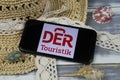 Closeup of smartphone with logo lettering of der touristik group travel agency with sun hat and shells on wood table