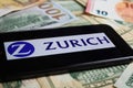 Closeup of smartphone with logo lettering of zurich insurance company on paper money currency