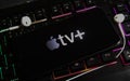 Closeup of smartphone screen with logo lettering of online tv and movie streaming service apple tv on illuminated computer keyboar