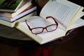 View on open book with red reading glasses and stack of travel books