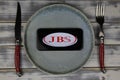 Closeup of mobile phone on plate and wood table, cutlery with logo lettering of Jose batista sobrinho JBS food company