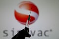 Close up of syringe hold by hand with injection needle and serum, blurred Sinovac logo lettering background