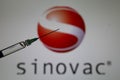 Close up of syringe with injection needle and serum, blurred Sinovac logo lettering background