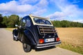 Rear view of black French classic cult car 2CV with open roof and wooden luggage rack in rural area against blue sky