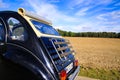 Rear view of black French classic cult car 2CV with open roof and wooden luggage rack in rural area against blue sky