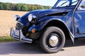 View on front wheel arch, tire, silver headlights and radiator grille of black French classic cult car 2CV in rural area