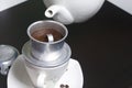 Vietnamese coffee maker is equipped on a cup. Ground coffee is poured into it. Barista pours boiling water from the teapot into it