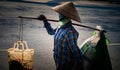 Vietnamese with conical hat carries a yoke on her shoulder along the street.