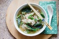 Pho Ga served in a white bowl on wooden board with a spoon. Turquoise dotted napkin.