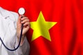 Vietnamese doctor's hand with stethoscope on the background of flag of Vietnam. Medicine, clinic, practitioner, healthcare