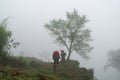 Vietnamese ethnic minority Red Dao women in traditional dress and basket on back with a tree in misty forest in Lao Cai, Vietnam